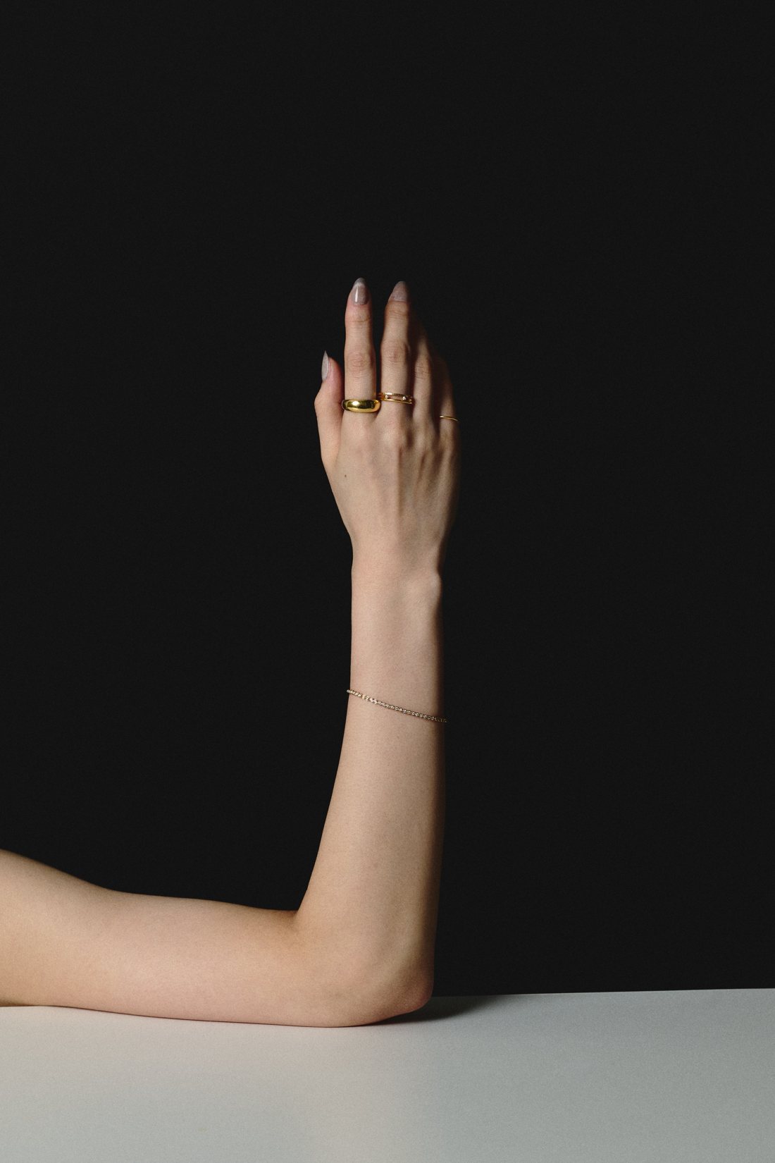 Raised arm wearing gold rings and a fine bracelet
