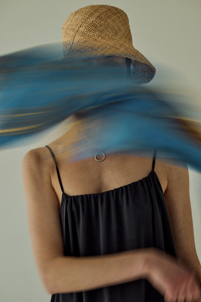 A figure in a straw hat behind a sweep of blue fabric