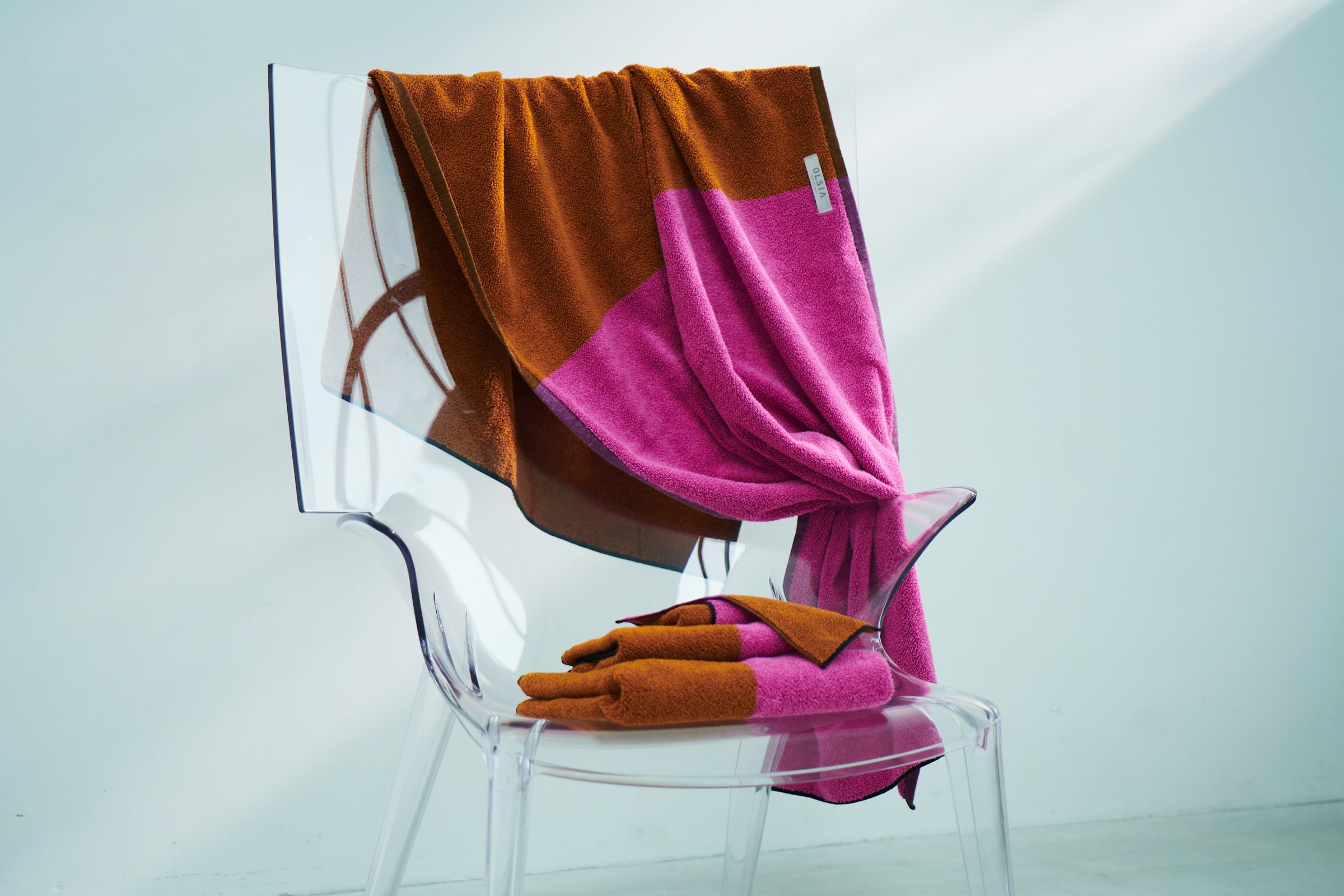 Towels in rust and pink draped over a clear acrylic chair