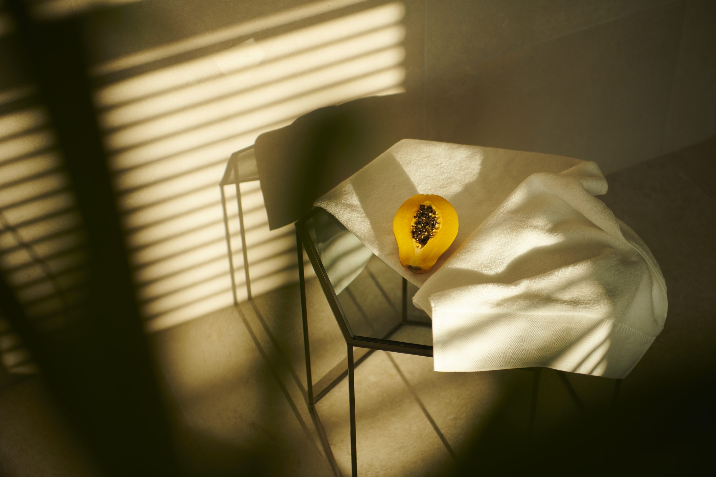 Half a papaya resting on a white towel in striped shadow
