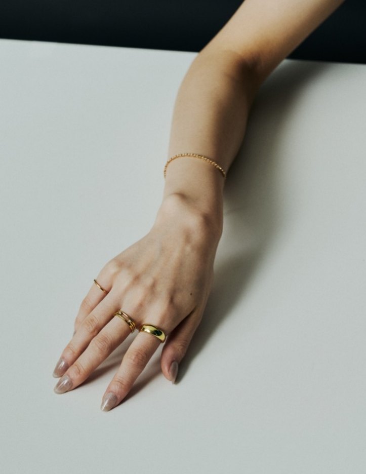 Hand with stacked gold rings and bracelet on a white surface