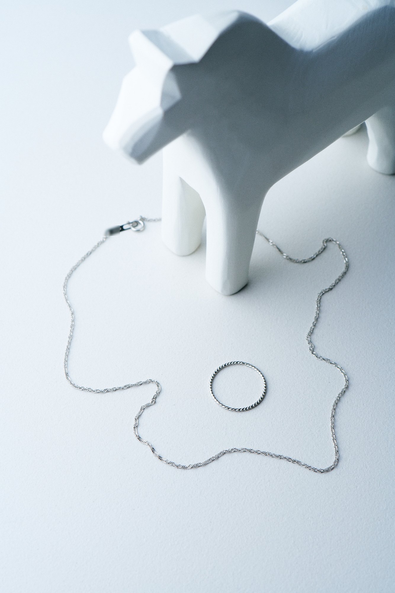 Silver chain and twisted ring beside a white carved horse