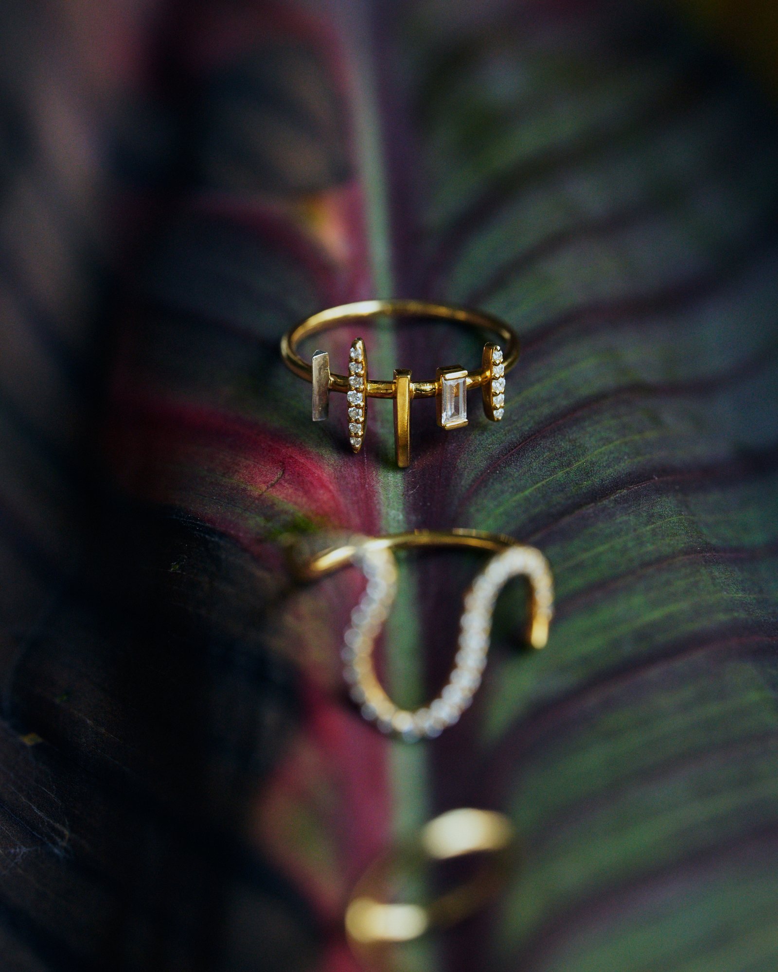 Gold bar ring with pavé and baguette stones on a dark leaf