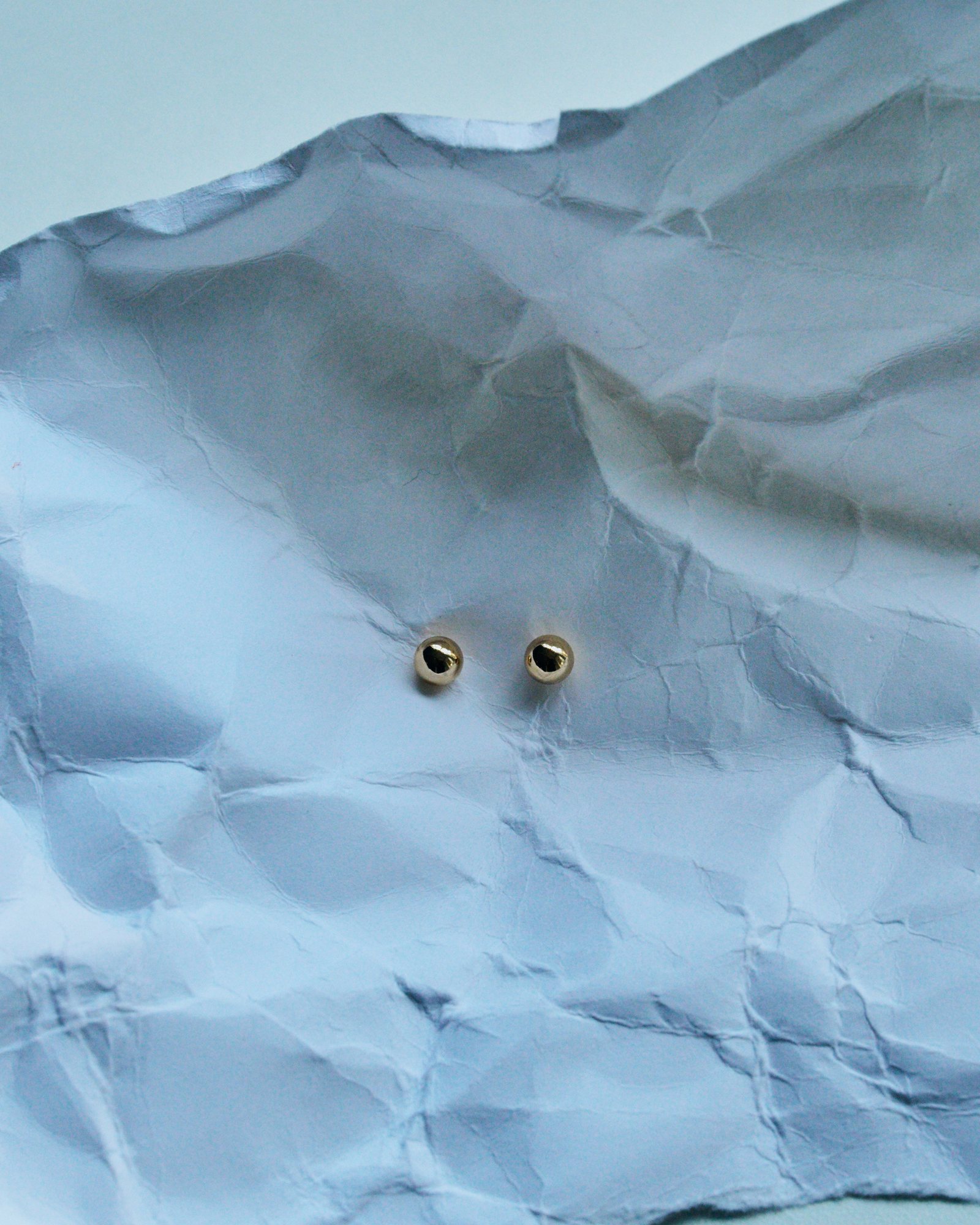 Gold ball stud earrings on crumpled pale blue paper