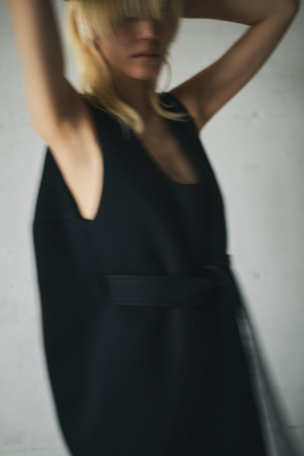 Motion-blurred portrait of a model in a black sleeveless dress with a wide belt