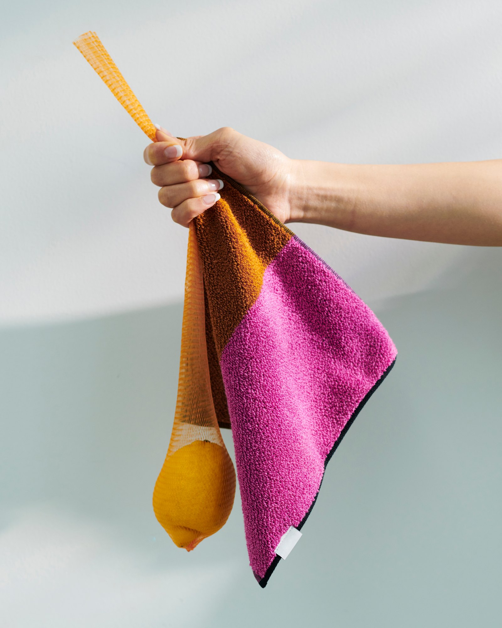 Hand holding a two-tone terry towel and a lemon in an orange net