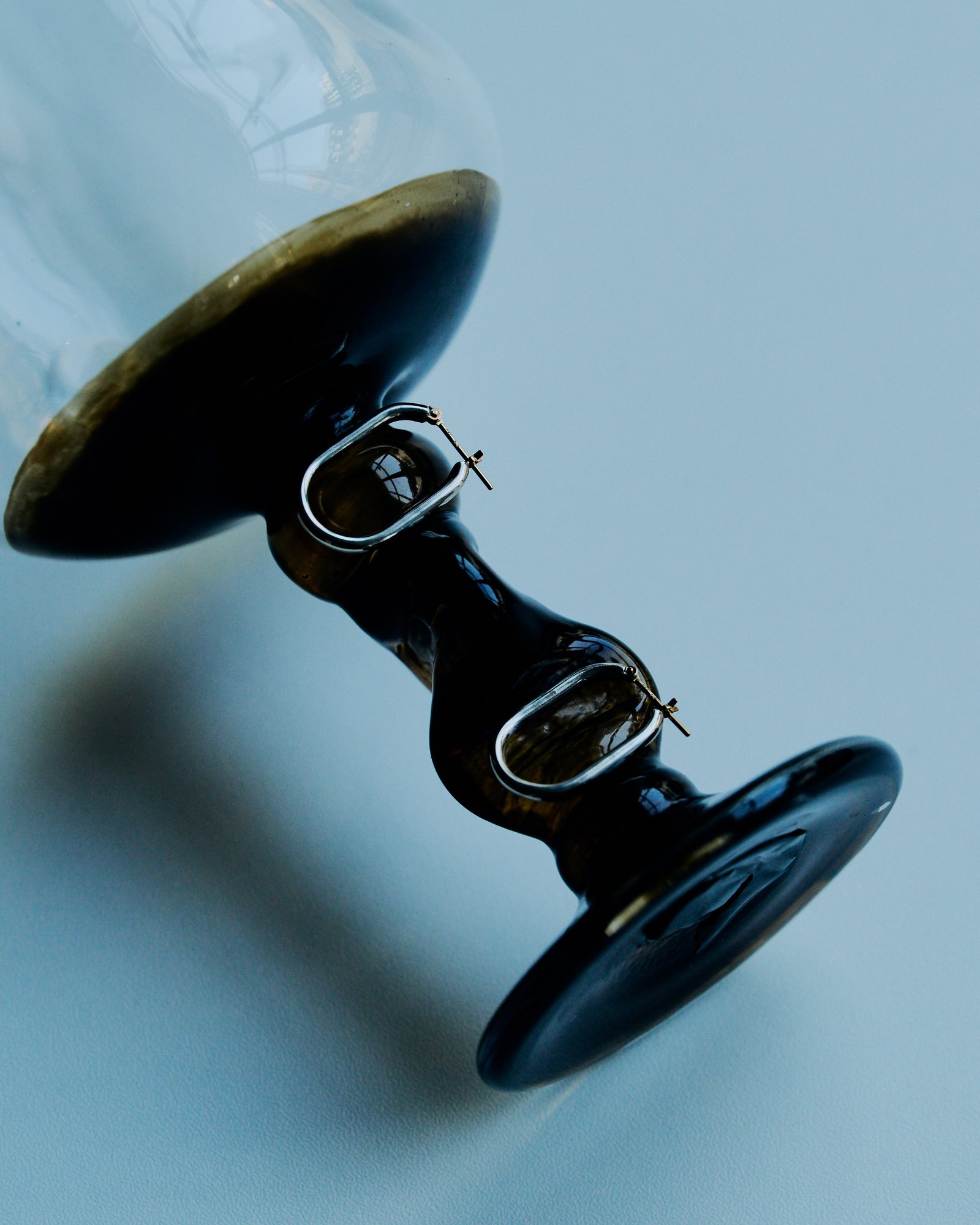 Silver hoop earrings on the stem of an amber glass vase