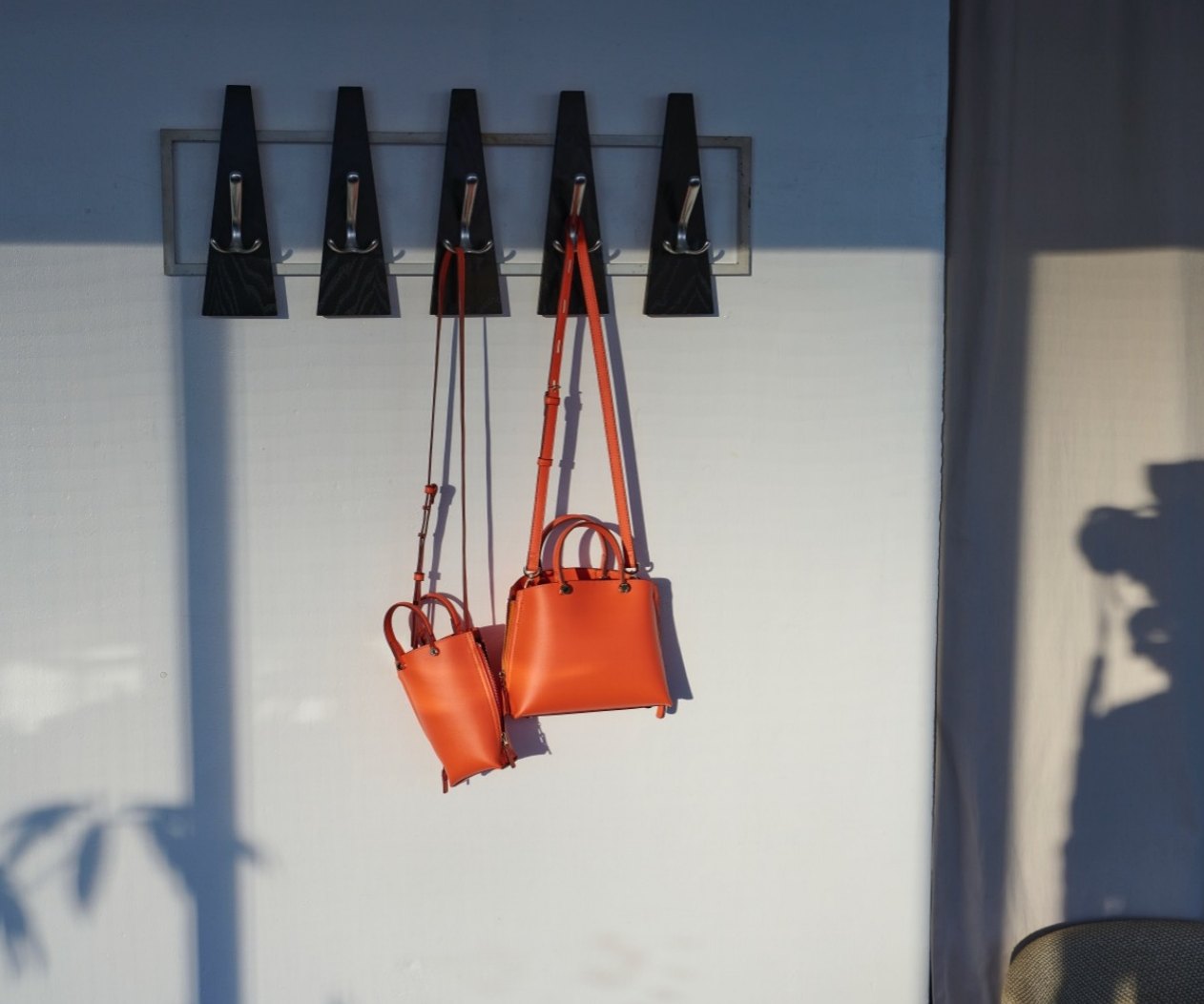 Orange bags hanging from wall hooks in sunlight