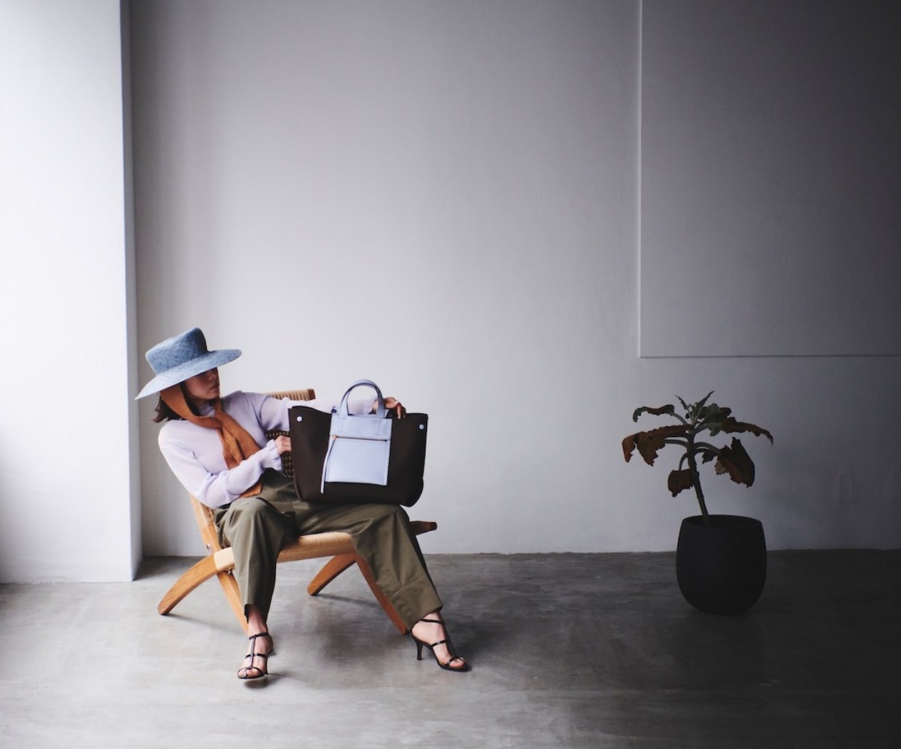 Woman in a wide-brim hat seated with a tote bag