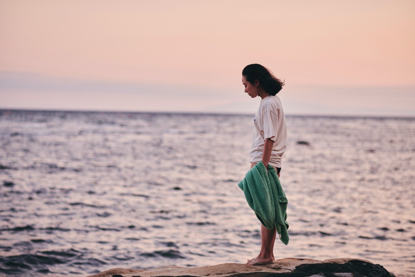 Woman holding a green towel on a rock by the sea at dusk